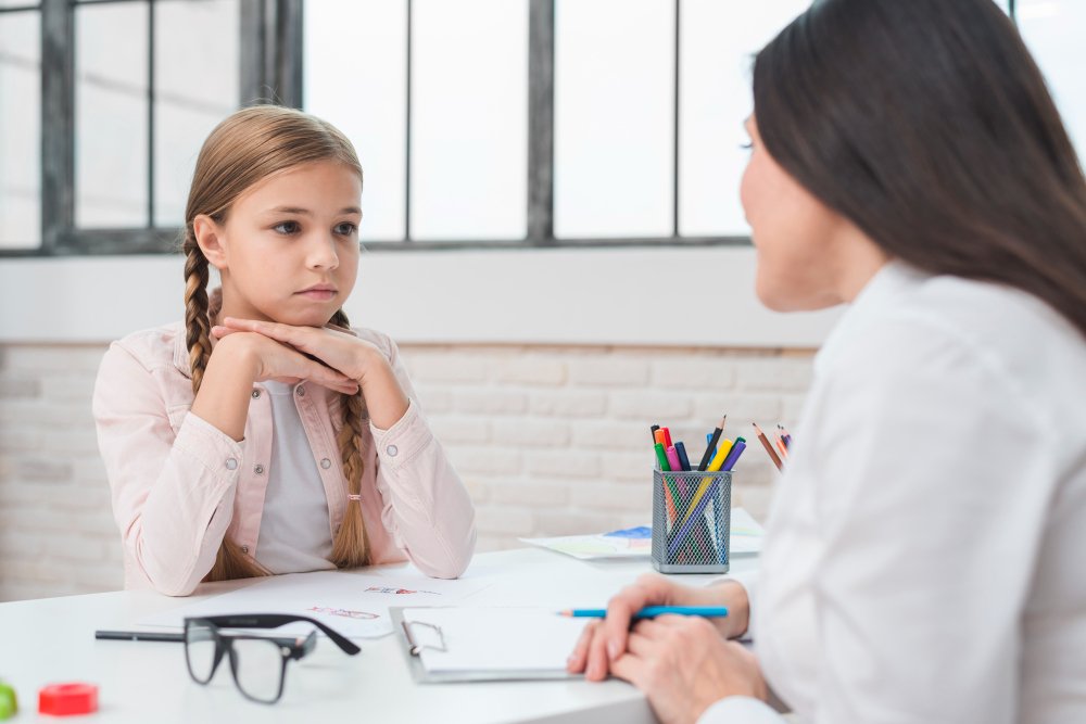 Criança com cara séria conversa com uma adulta em uma escola: problemas de saúde mental não tratados têm consequências negativas durante a vida